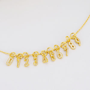 Gold number pendant necklace featuring diamond-encrusted 0-9 charms on a delicate chain.