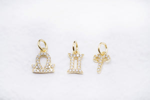 Diamond zodiac charms: Libra, Gemini, and Aries gold pendants on white.