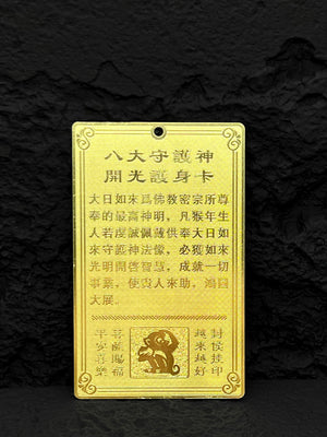 Gold amulet card with Chinese text detailing benefits for those born in the Year of the Monkey. Features decorative borders, monkey image, and hole for hanging.
