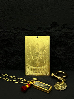 Gold Buddhist amulet necklace with seated Buddha, Chinese text, charms, and red tassel on black background. Spiritual, elegant Buddhist prayer beads.