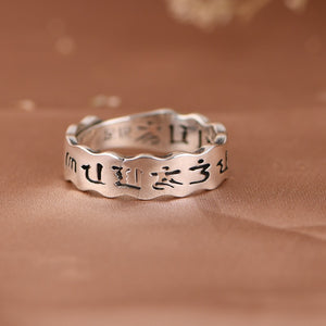 Close-up of elegant silver Tibetan ring with engraved script on a wavy band. Simple style, showcasing texture and detail.