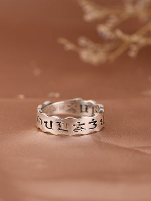 Elegant silver Tibetan ring with wavy band inscribed with Tibetan script on warm fabric.