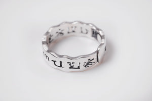 Close-up of a minimalist silver Tibetan ring with a wavy band. Chinese characters engraved inside and out.