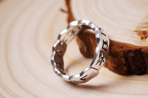 Close-up of elegant silver Tibetan ring with wavy design and engraved Chinese characters, resting on wood.