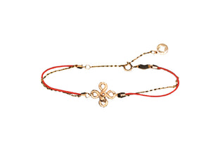Elegant gold bracelet with knotted design, red cord accents, and small charm. Minimalist Tibetan style.