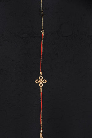 Elegant gold & red string bracelet with quatrefoil charm on black background. Minimalist Tibetan Buddhist prayer beads.
