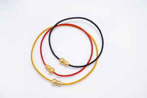 Three braided cord bracelets with gold dzi beads intertwined. Red, black, and gold color options. Tibetan dzi bracelet.