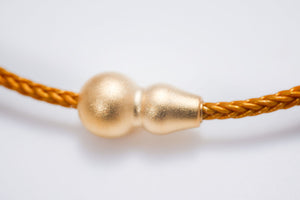 Close-up of a matte gold gourd-shaped Tibetan dzi bead on a braided gold cord. Minimalist style, perfect for Tibetan dzi stone beads lovers.