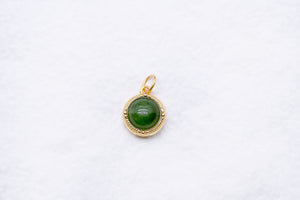 Gold pendant featuring a green stone. Beaded gold bezel with a loop for hanging. Jewelry close-up on a white surface.