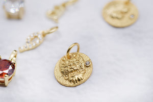 Gold pendants featuring a lion head relief with diamond, red gemstone, and embossed designs on marble.