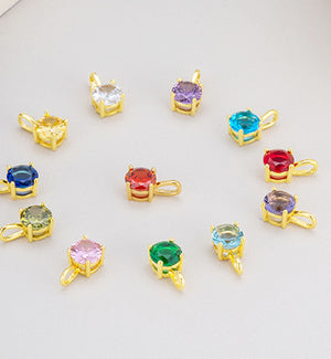 Colorful gemstone pendants in assorted colors. Faceted gems set in gold frames, arranged on a light gray background.