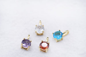 Four gold pendants with colorful gemstones: cubic zirconia, blue, purple, and orange on a white background. Sparkling gemstone jewelry.