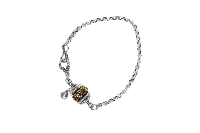 Sterling silver Tibetan prayer wheel bracelet on white background. Intricate two-toned pendant with gold detail. Fosters inner peace, protection.