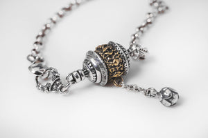 Elegant silver & gold Tibetan prayer wheel pendant bracelet. Close-up detail showcases intricate gold work & spiritual charm on chunky chain.