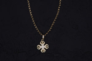 Elegant gold Dharma Wheel pendant necklace with sparkling gems on a curb chain. Tibetan Buddhist amulet on a textured black background.