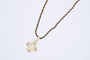 Elegant gold flower pendant necklace with inlaid crystals and a unique black cord and gold link chain. Tibetan dzi beads inspire this minimalist design.