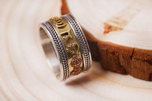 Close-up of elegant Tibetan prayer ring with silver, gold, and copper details. Intricate braiding and inscription showcase craftsmanship.