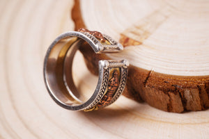 Close-up of intricate silver and copper Tibetan ring on wood. Adjustable design featuring a small figure.