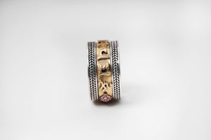 Close-up of Tibetan spinning ring with silver herringbone bands, gold script, and copper symbol. Unique Tibetan jewelry on white background.