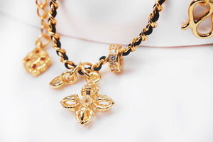 Elegant gold charm bracelet with black cord featuring fleur-de-lis, heart, and other symbolic charms. Buddhist prayer beads for a vintage-inspired look.