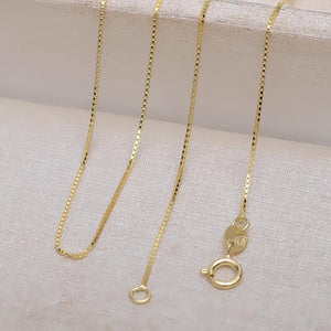 Elegant gold box chain necklace on off-white background. 585 hallmark visible. Minimalist style, perfect for everyday wear.