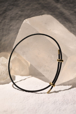 Minimalist necklace with black cord, gold accents, and crystal background. A stylish jewelry piece.