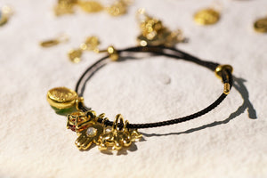 Black cord charm bracelet with gold charms on white textured surface.