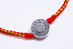 Close-up of a red and gold braided Tibetan dzi beads bracelet with a silver astrological charm on a white background.