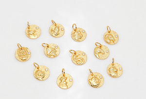 Gold zodiac pendants. Circular charms with embossed zodiac symbols and gem details arranged on a white background.
