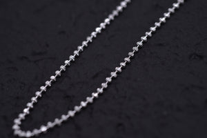 Close-up of delicate silver ball chain sparkling against a textured black background. Elegant, simple style. Tibetan dzi beads.