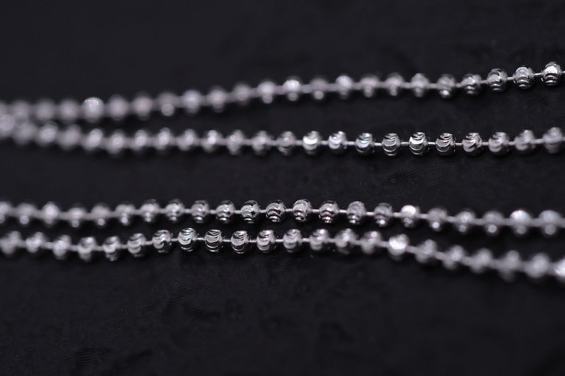 Gleaming silver Tibetan dzi beads layered against black fabric. Close-up showcases intricate detail and textured shine.
