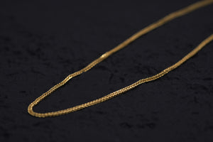 Close-up of a delicate, intricate gold franco chain. Warm lighting showcases its craftsmanship against a dark background.
