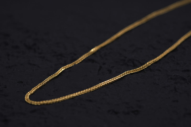 Close-up of a delicate, intricate gold franco chain. Warm lighting showcases its craftsmanship against a dark background.