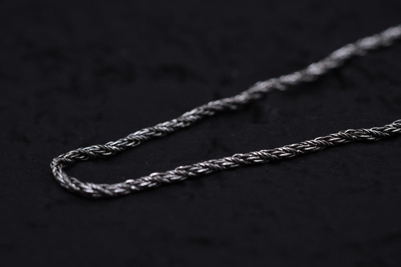 Close-up of antique silver braided chain on black background. Rustic Tibetan bracelet detail.
