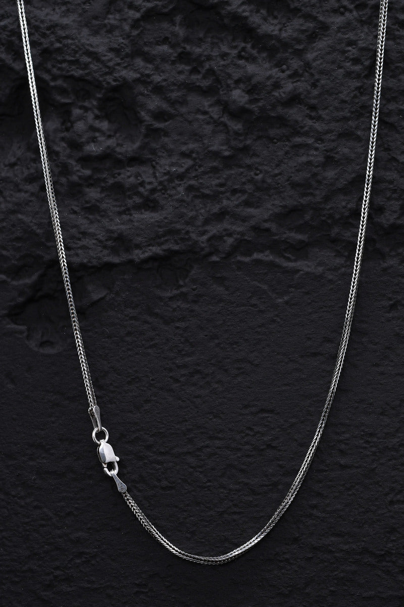 Close-up of a gleaming sterling silver snake link necklace on a black background. Classic lobster clasp.
