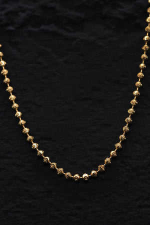 Close-up of a thin, gold-plated sterling silver cut ball chain necklace. The textured beads shine against a black background.