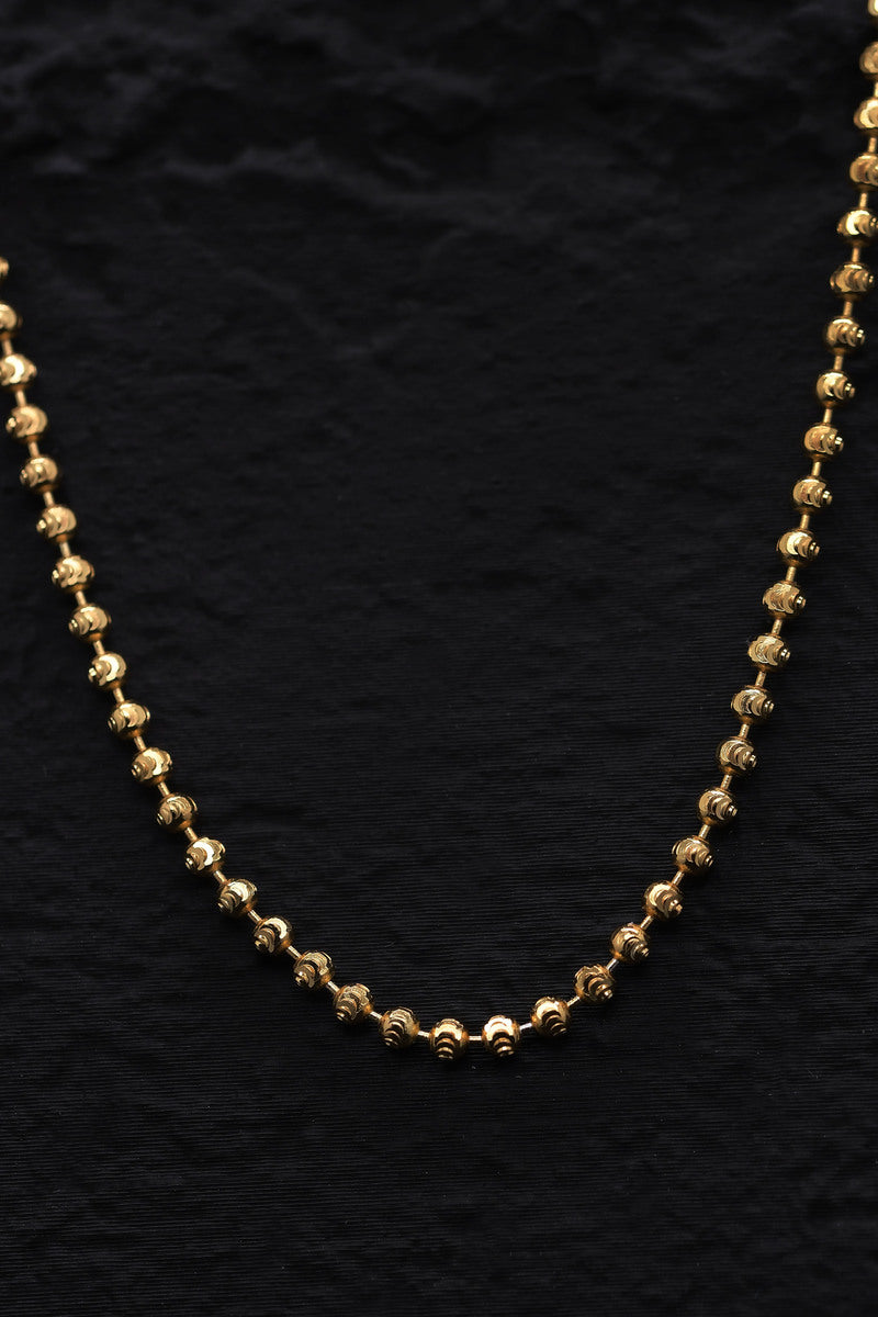 Close-up of a thin, gold-plated sterling silver cut ball chain necklace. The textured beads shine against a black background.