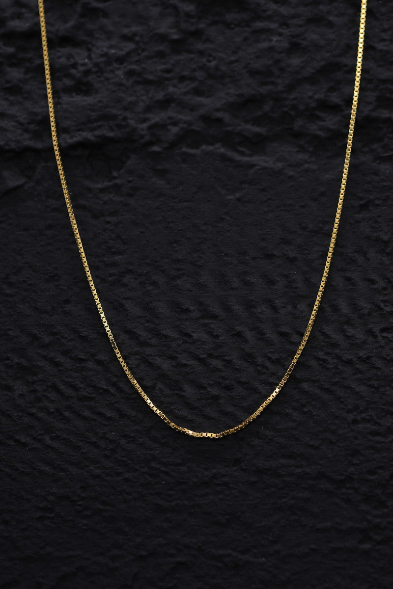 Close-up of a gleaming gold tone box chain necklace against a black background. Delicate craftsmanship shines. Sterling silver necklace.