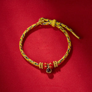 Braided cord bracelet with red beads, gold spacers, and a dark stone charm. Sliding clasp. Colorful woven bracelet detail.