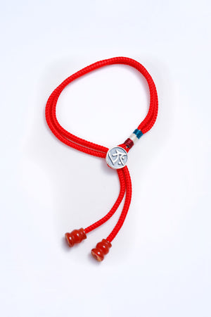 Red braided cord bracelet with silver charm and colorful threads. Adjustable sliding knot closure. Minimalist Tibetan Buddhist prayer beads style.