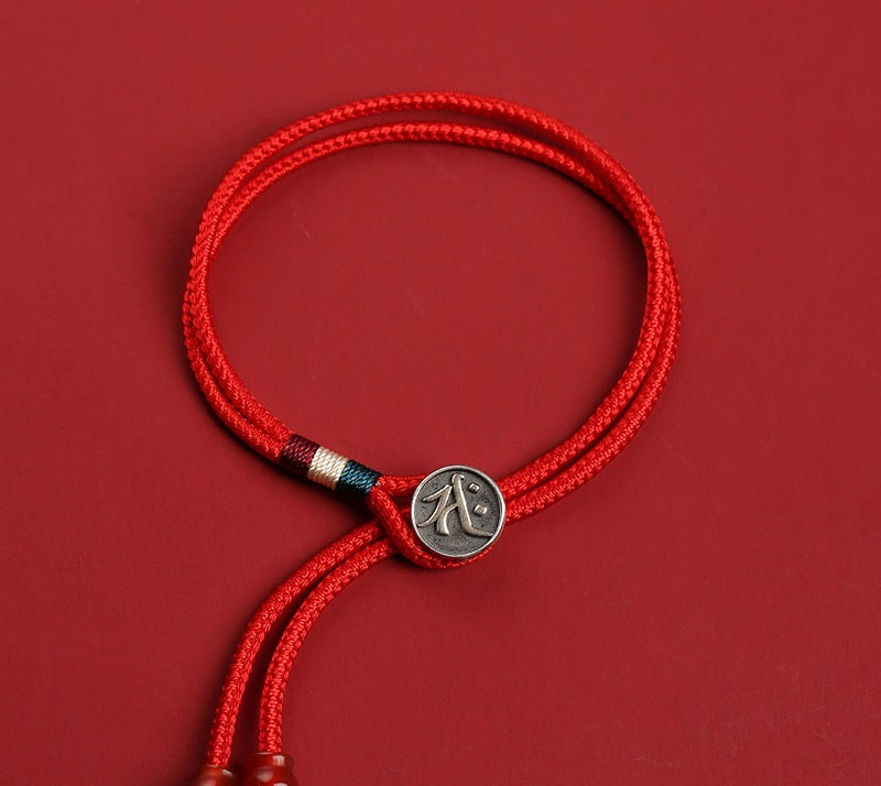 Elegant red braided cord bracelet with silver charm featuring a Chinese eternity symbol. Tibetan dzi beads accent the adjustable cord.