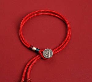 Red braided cord bracelet with silver Om medallion and colorful beads. Tibetan dzi beads add a spiritual touch to this minimalist style.