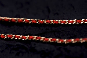Gold chain with red thread accents on dark background. Elegant Tibetan Buddhist prayer beads.