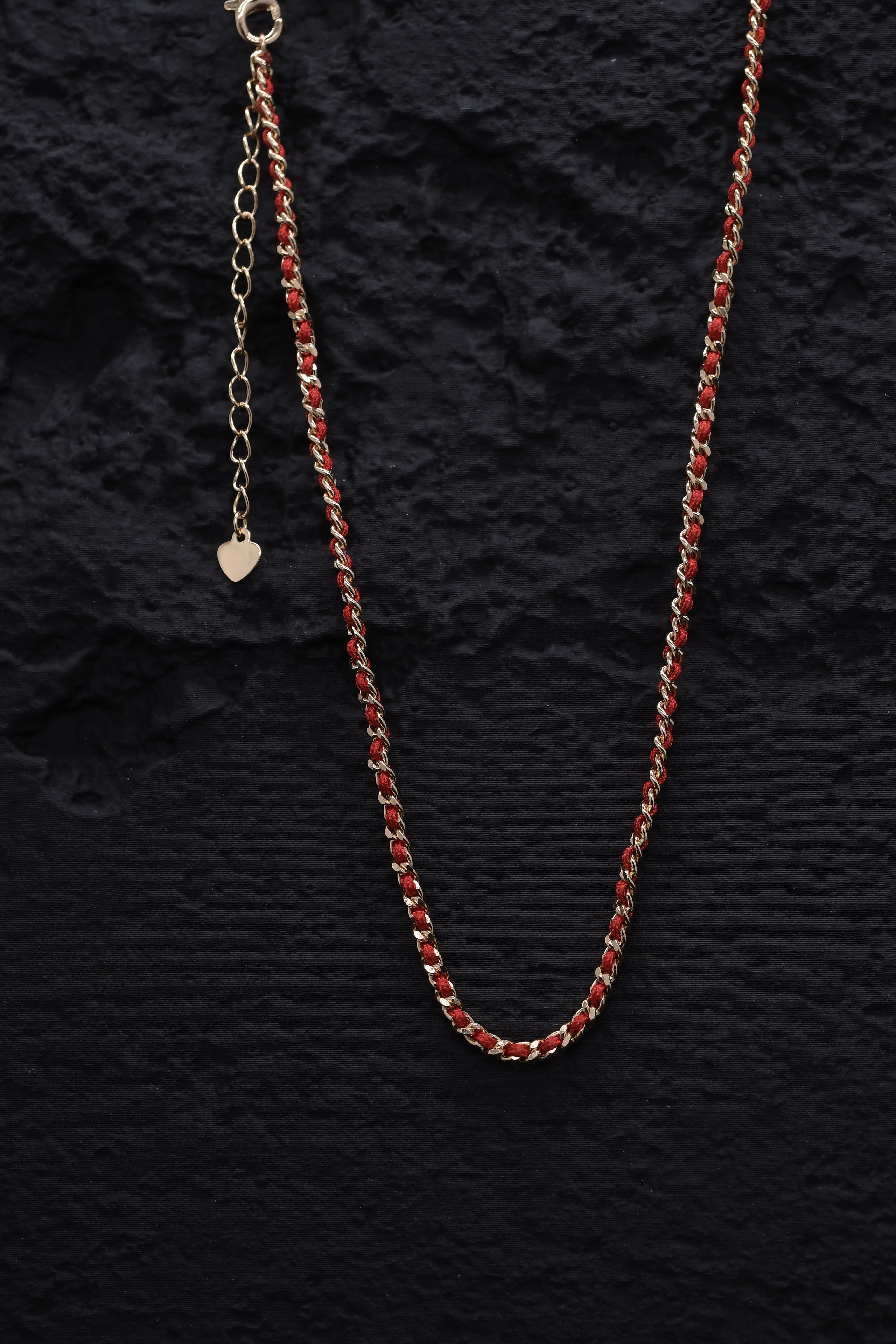 Elegant gold chain necklace with red thread accent and heart charm on black background. Tibetan Buddhist prayer beads style.