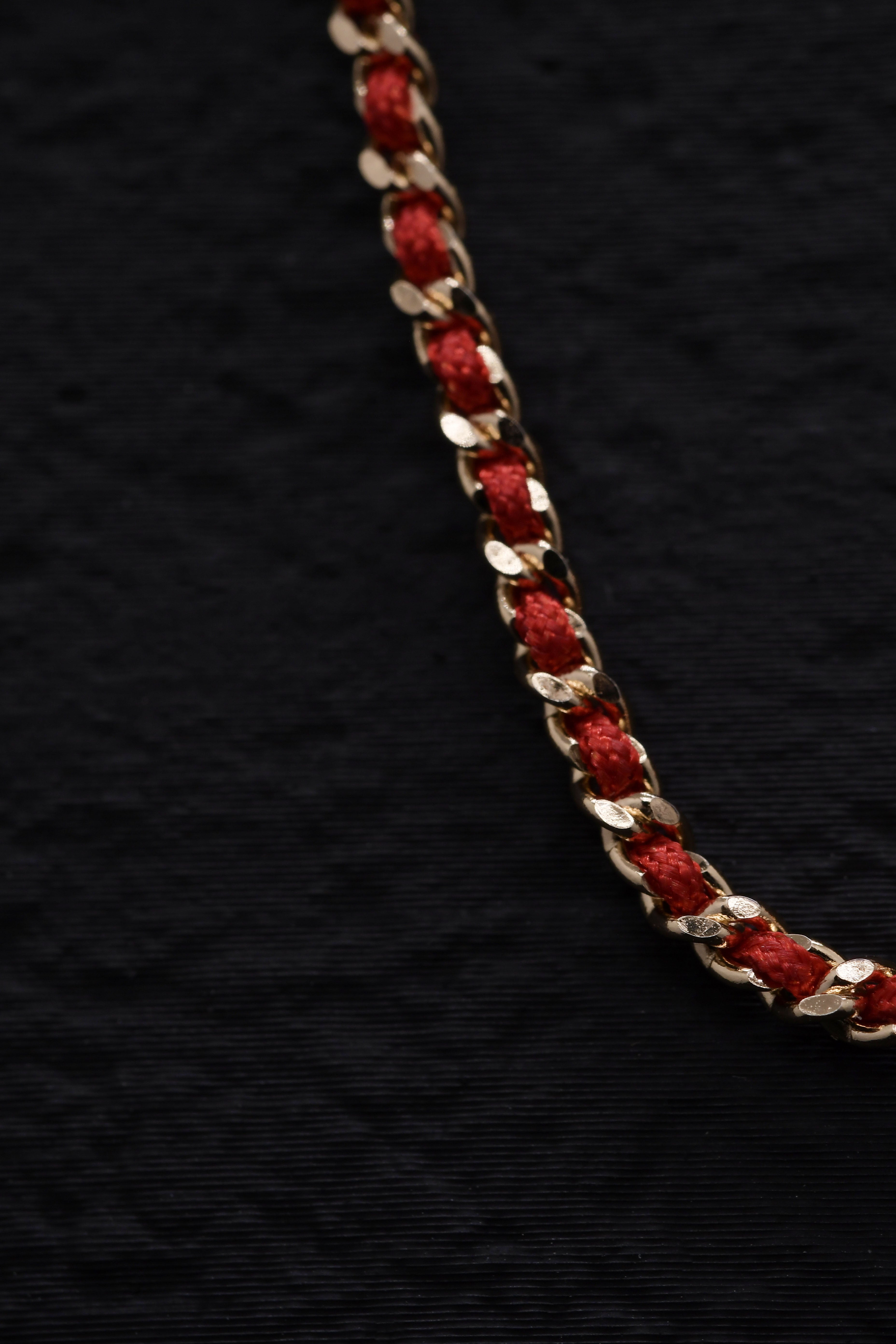 Gold chain with red woven cord against a black background. Tibetan prayer beads mala with unique oval links.