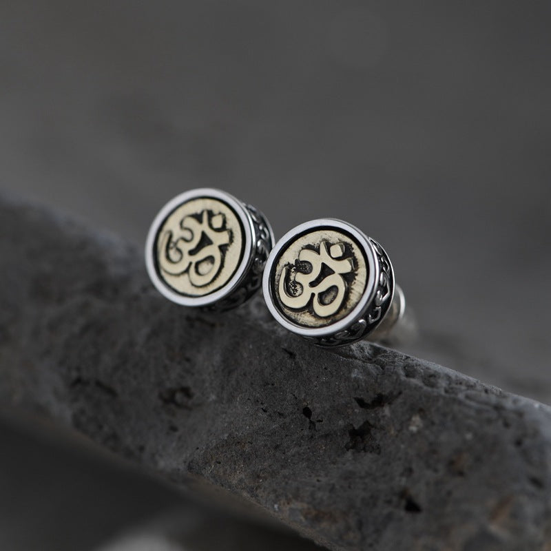 Silver Om stud earrings with textured, beaded borders on dark stone. Simple, spiritual Tibetan Buddhist style.