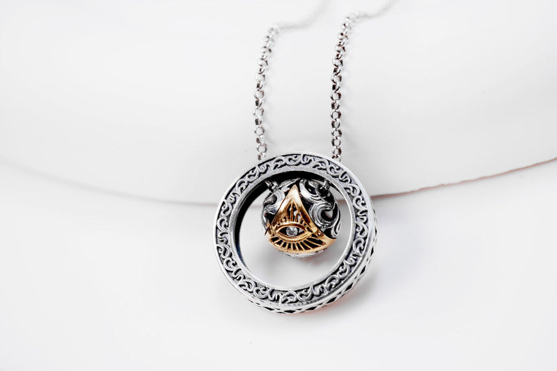 Close-up of elegant silver & gold pendant necklace featuring a textured sphere and crystal. Tibetan dzi bead-inspired design with ornate detailing.