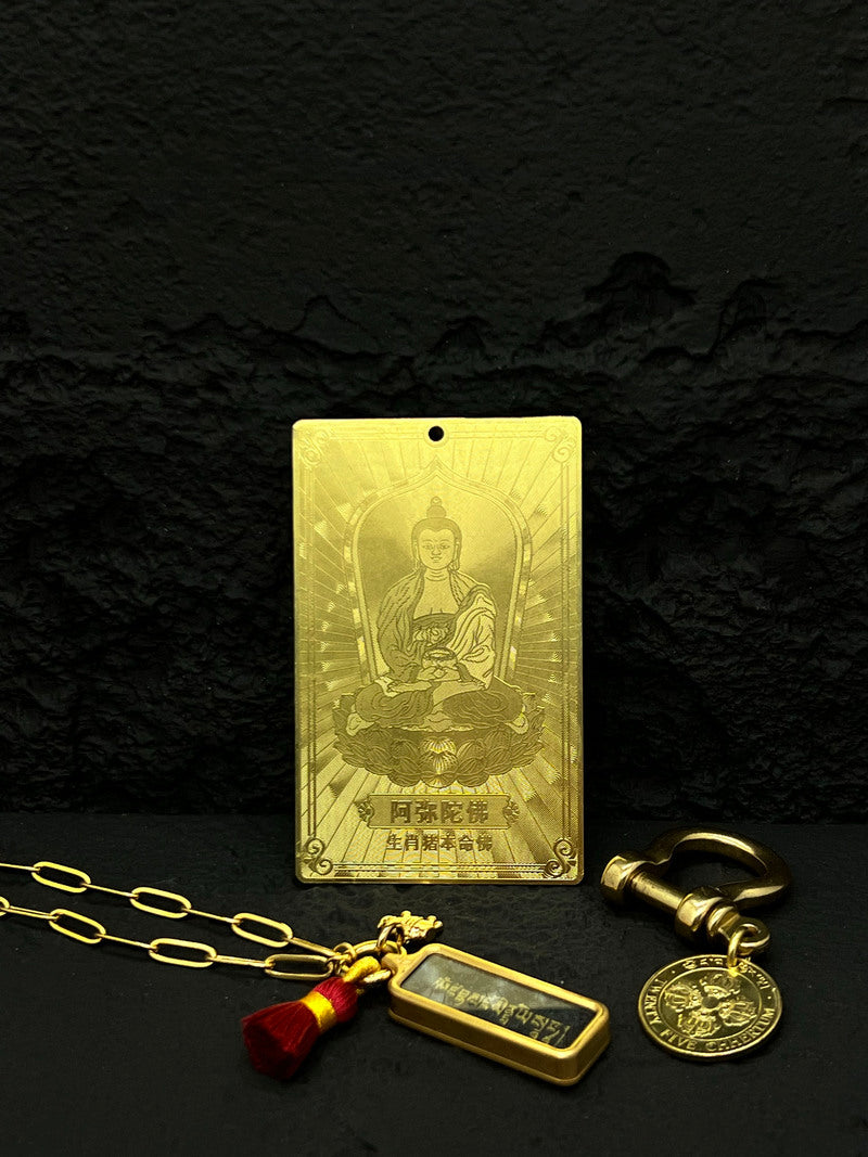 Gold Buddhist amulet necklace with seated Buddha, Chinese text, charms, and red tassel on black background. Spiritual, elegant Buddhist prayer beads.