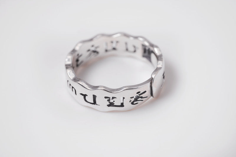 Close-up of a minimalist silver Tibetan ring with a wavy band. Chinese characters engraved inside and out.