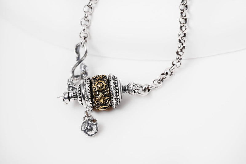 Silver & gold Tibetan prayer wheel pendant necklace on delicate chain. Intricate etched details, minimalist style, spiritual jewelry.
